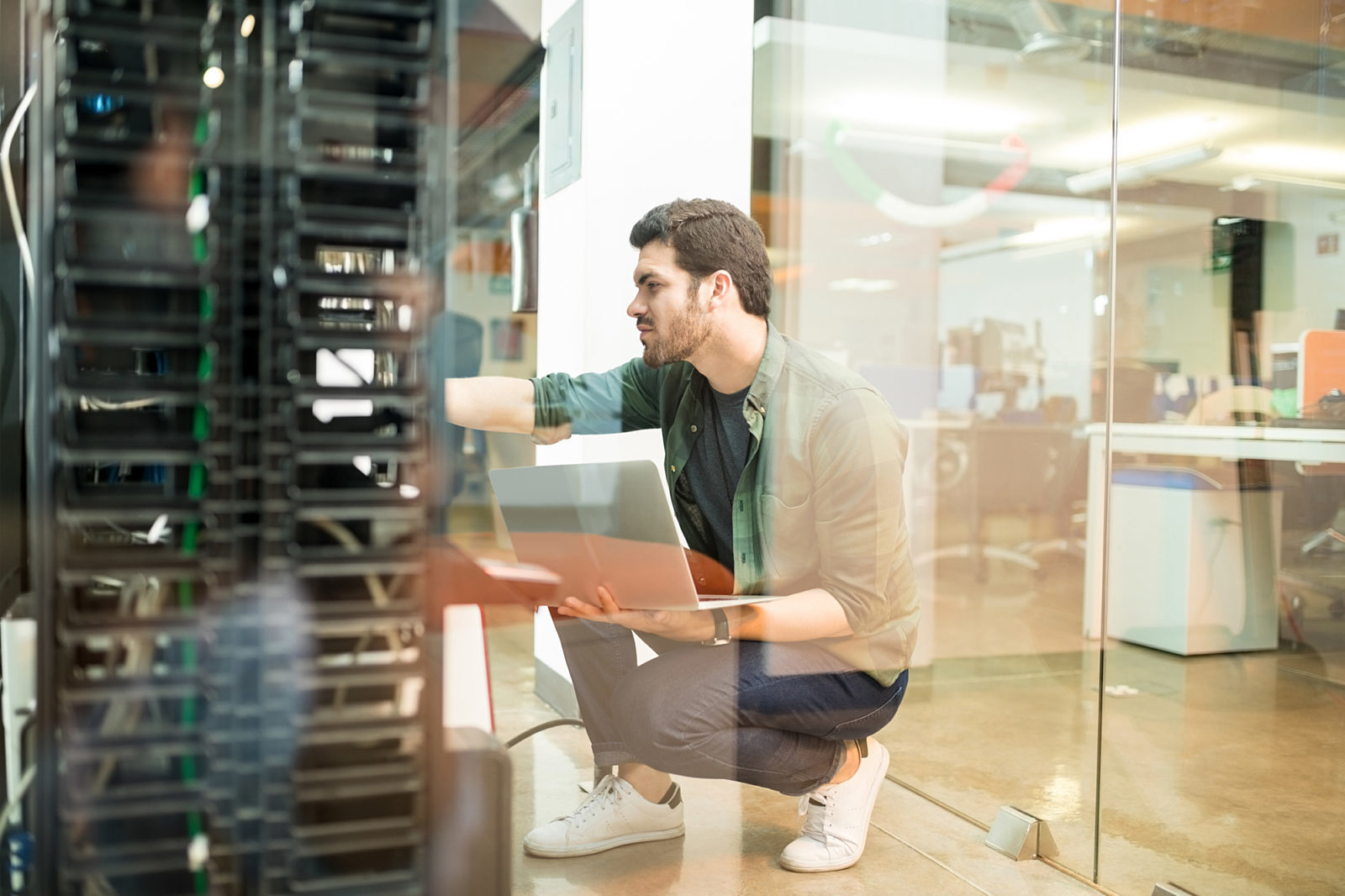 A technician working in a modern server room, holding a laptop and checking hardware connections, reflecting IT infrastructure management in a workspace.