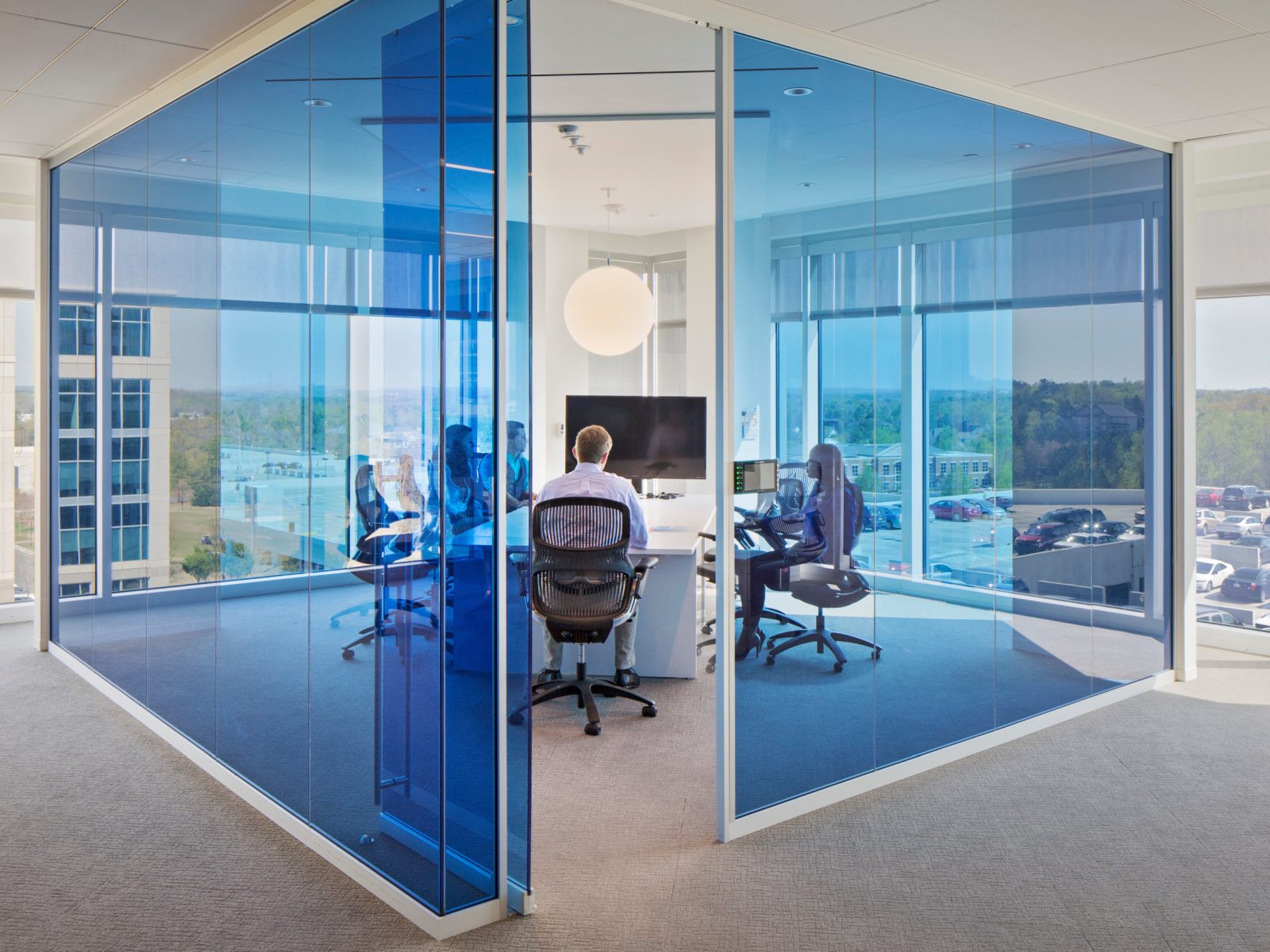 Symbio walls with vibrant blue glass create private, light-filled meeting spaces in a contemporary office, blending openness with acoustic privacy.