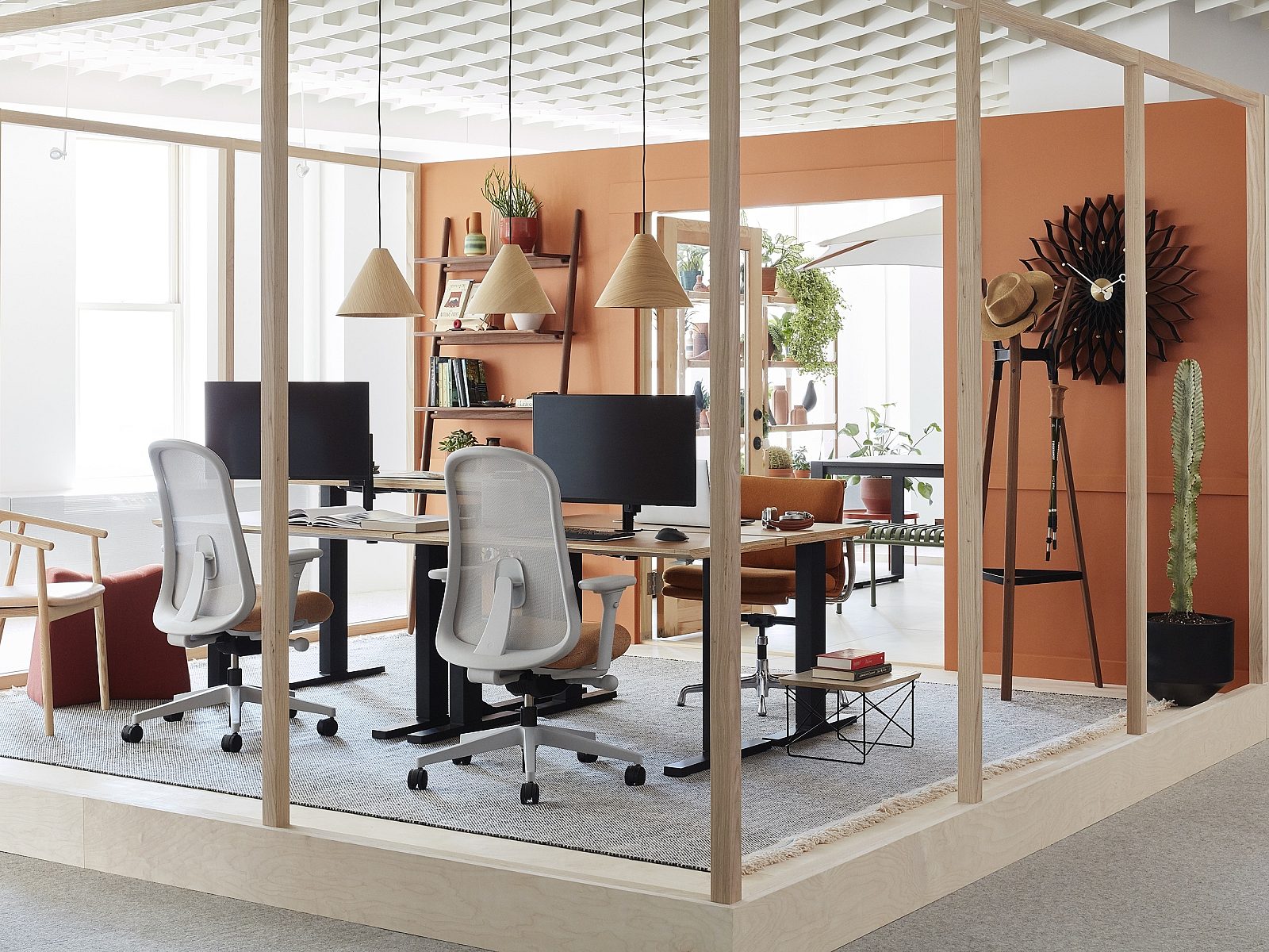 Modern office space with wood framing, ergonomic chairs, computer monitors, and warm orange accents. Shelves with greenery and decor create a cozy vibe.