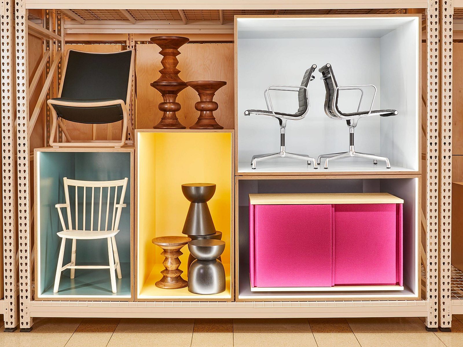 Furniture and decor displayed in colorful cubed shelves, featuring chairs, stools, and storage units in sections of blue, yellow, pink, and neutral tones.