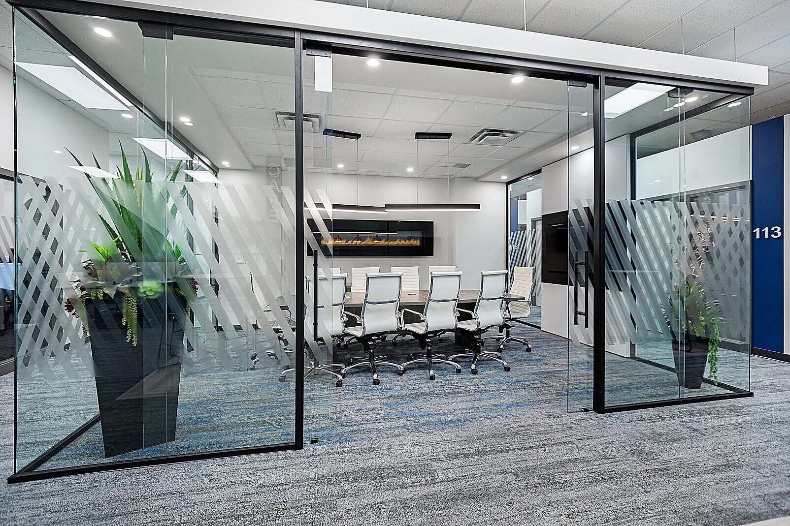Falkbuilt walls showcase this glass-enclosed conference room with frosted diagonal patterns, modern white chairs, a wood table, and blue accent walls.