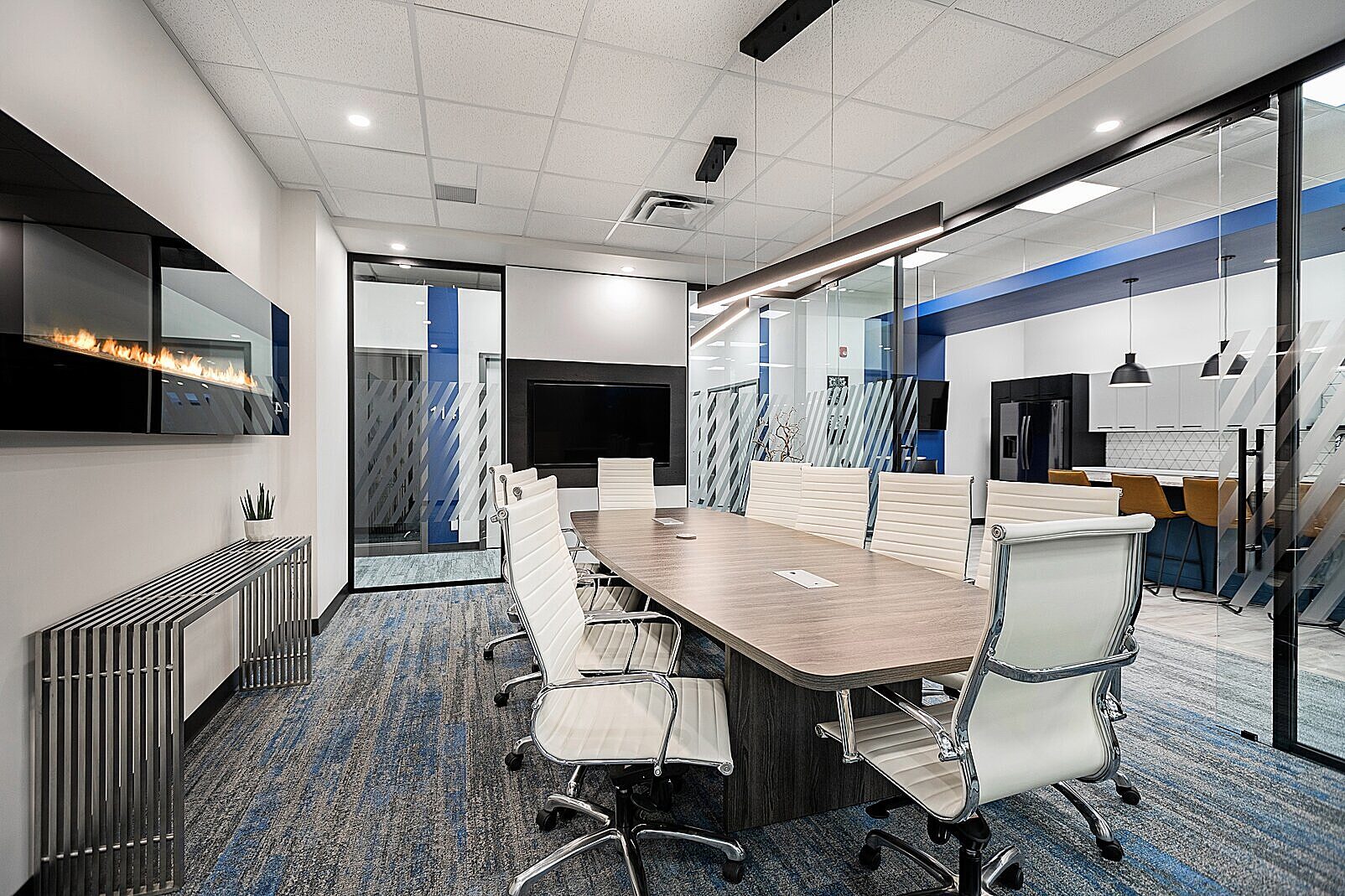 Falkbuilt walls define this sleek conference room with glass panels, blue accents, and a modern aesthetic, featuring white chairs and a central wood table.