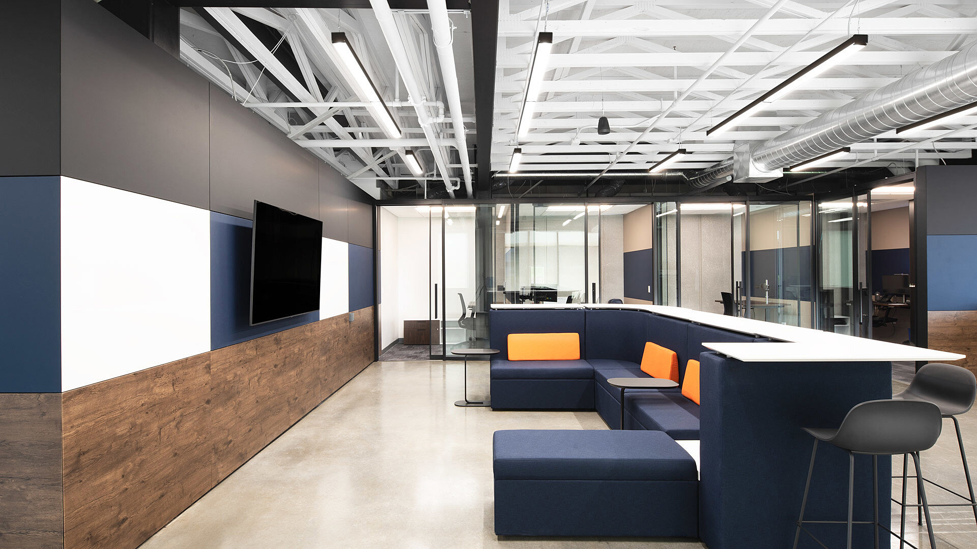 Falkbuilt walls shape this office with wood accents, glass partitions, and a seating area featuring blue and orange furniture under an exposed ceiling.