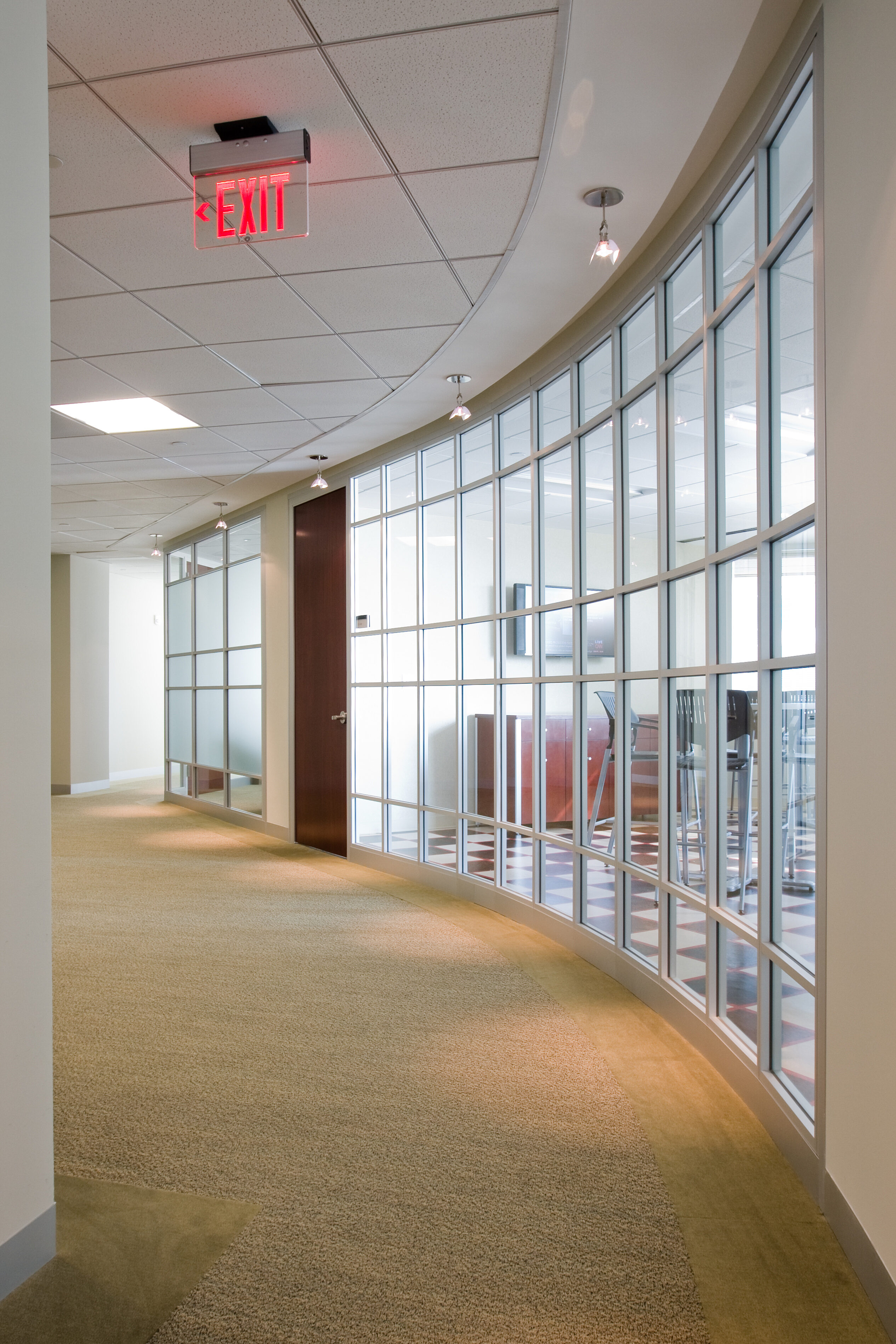 Curved Symbio glass walls create a sleek, open corridor with natural light streaming into adjacent rooms. The design blends transparency and functionality.