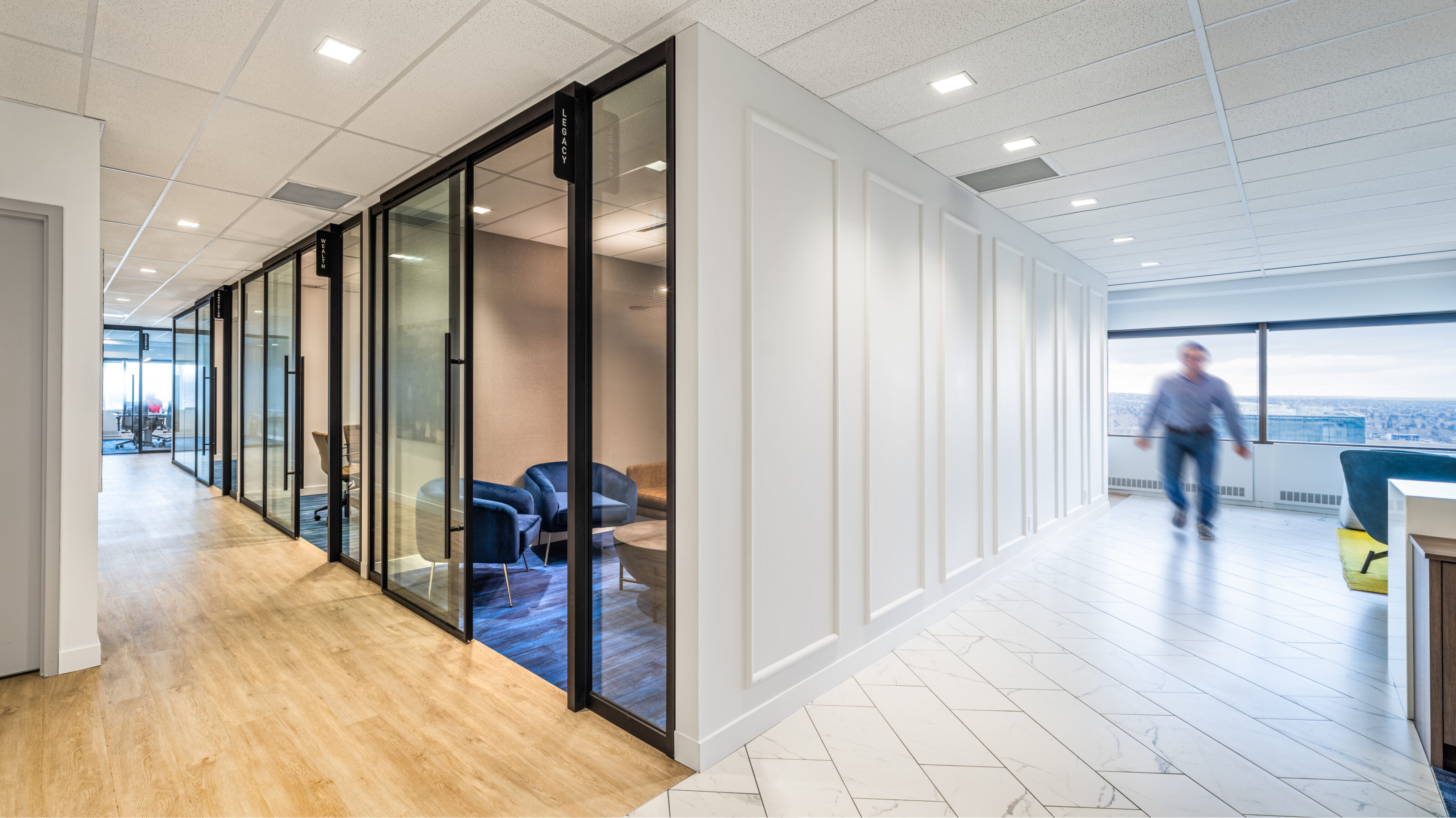 Falkbuilt office space featuring glass-walled meeting rooms, white paneled walls, light wood and tile flooring, with expansive views in the background.