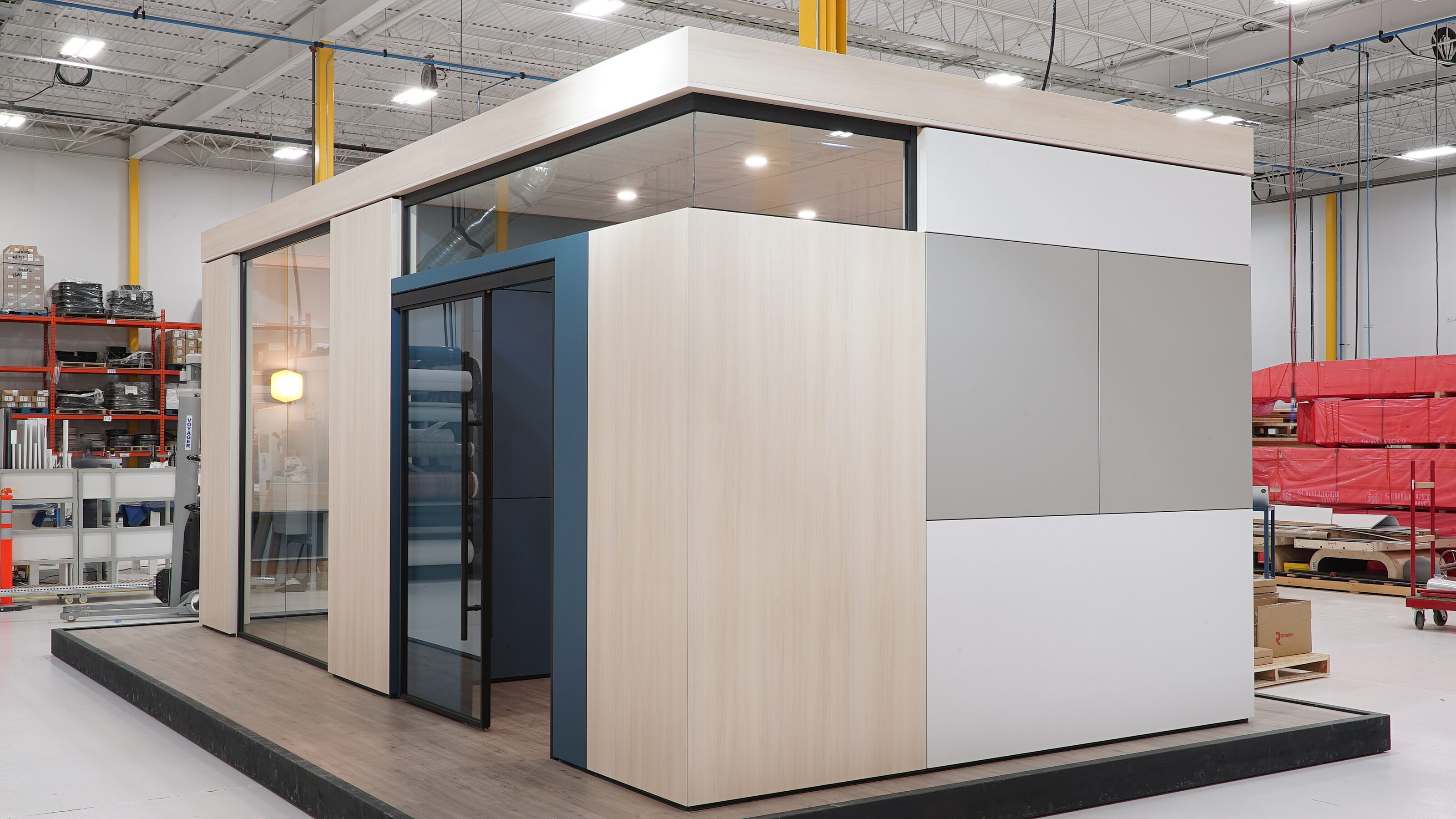 Falkbuilt modular structure featuring light wood and white panels, glass doors, and a modern design, showcased in a warehouse with industrial elements.