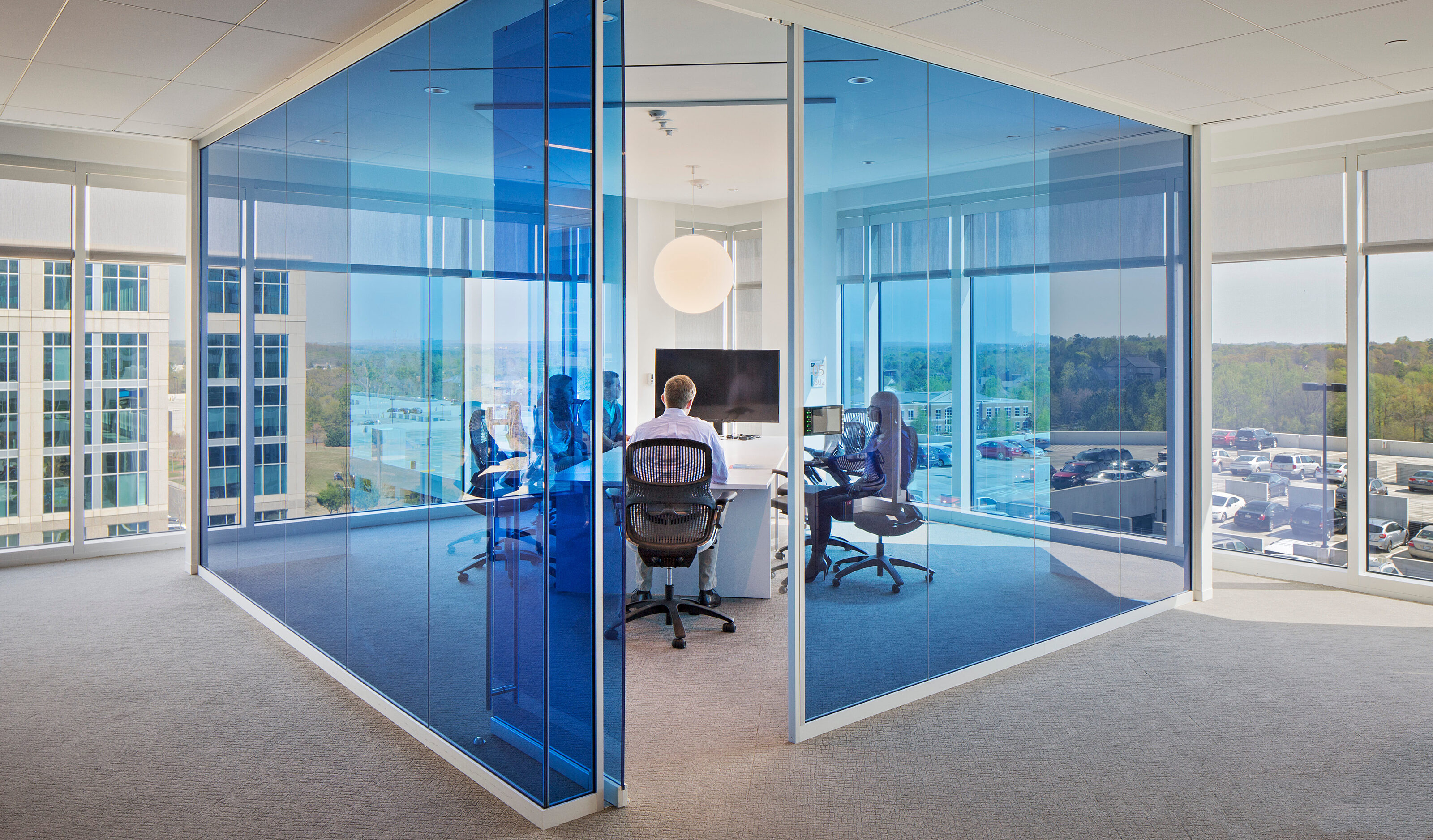 Symbio walls with vibrant blue glass create private, light-filled meeting spaces in a contemporary office, blending openness with acoustic privacy.