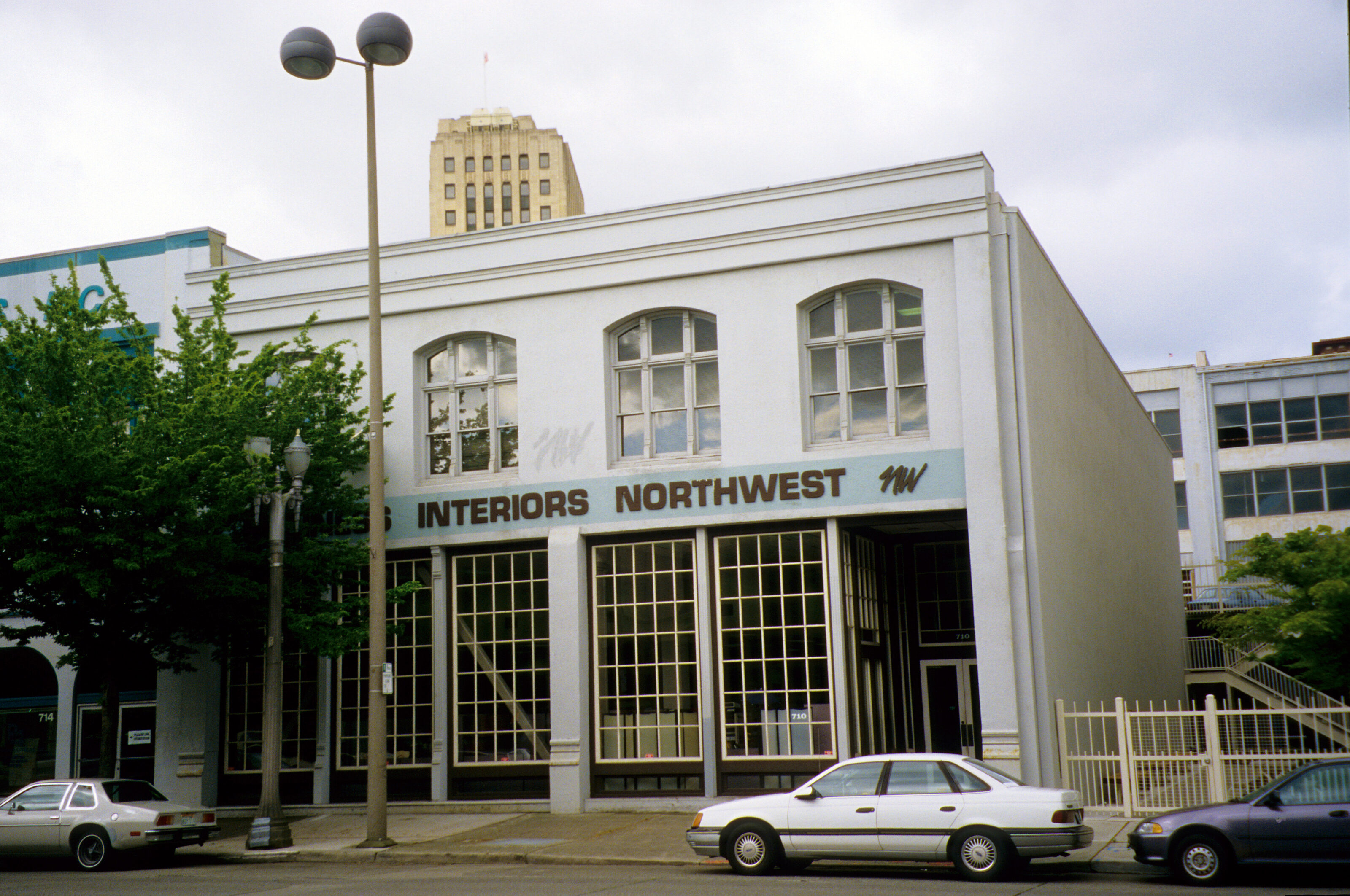A vintage two-story building with "Business Interiors Northwest" signage, large arched windows, and parked cars in front, located in an Downtown Tacoma.