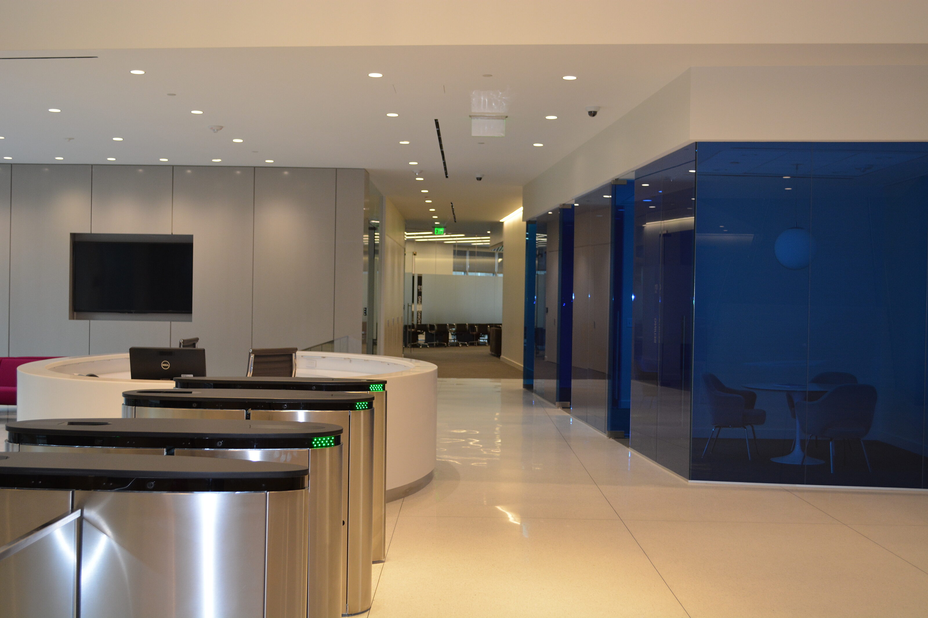 Modern office lobby featuring Symbio glass walls, including vibrant blue partitions, and a sleek curved reception desk blending design with functionality.