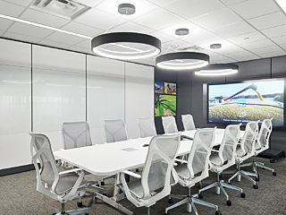A modern conference room featuring ergonomic white chairs, a sleek table, circular pendant lights, and a large display screen showcasing digital content.