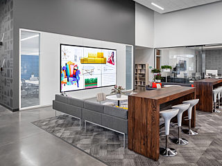 A contemporary workspace featuring a high-definition display showcasing colorful design concepts, a cozy gray sofa, and a wooden table with stools.