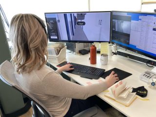 A person works at a desk with dual monitors, designing a walls project. The workspace includes a keyboard, water bottle, and various office supplies.