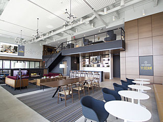 Modern lounge area with a mix of seating, tables, and a fireplace, featuring high ceilings, an upper level, and digital displays enhancing the environment.