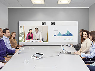 A conference room equipped with Cisco technology, featuring a video conferencing system, large display, and participants using tablets and laptops.
