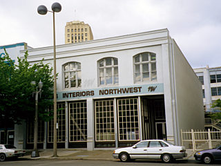A vintage two-story building with "Business Interiors Northwest" signage, large arched windows, and parked cars in front, located in an Downtown Tacoma.