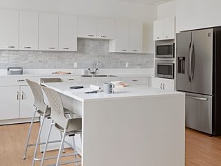 Staff break room, white laminate Mora casework along backwall & an island of white Mora casework with 2 Caper stools in Cappuccino seat/back, silver legs.