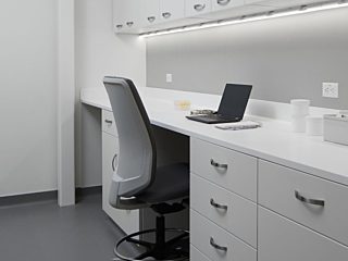 Laboratory workspace with white Mora casework for upper and lower cabinets and a Verus stool in a gray upholstery.