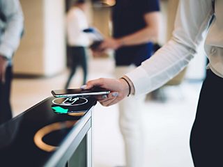 Close-up of a person using a smartphone to scan a digital access point, showcasing modern contactless entry technology in a sleek office environment.