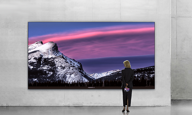 A sleek, high-definition MAXHUB display showcasing a vibrant mountain landscape with purple and pink skies, viewed by a person in a professional setting.