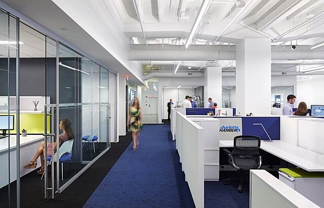 Glass Symbio walls create quiet workspaces in an open office, blending transparency with sound isolation. Features bright colors and modern furnishings.