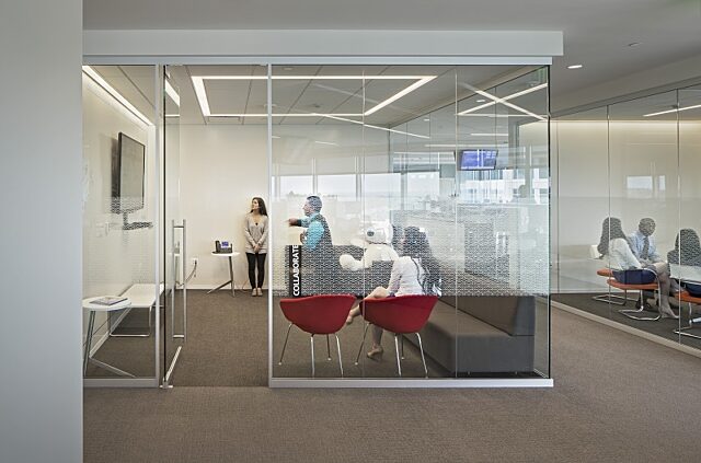 Symbio glass walls define collaborative spaces with frosted patterns for privacy, modern seating, and natural light creating a functional meeting area.