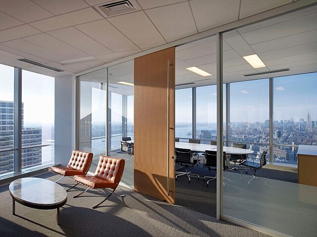 Conference room and lounge featuring Symbio walls with a large wood sliding door, floor-to-ceiling windows offering city views, and modern furniture.