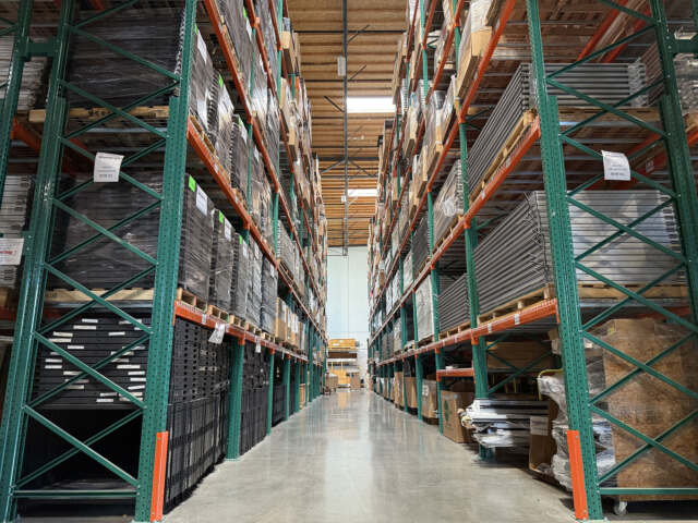 Warehouse aisle with tall shelves stacked with pallets of materials.