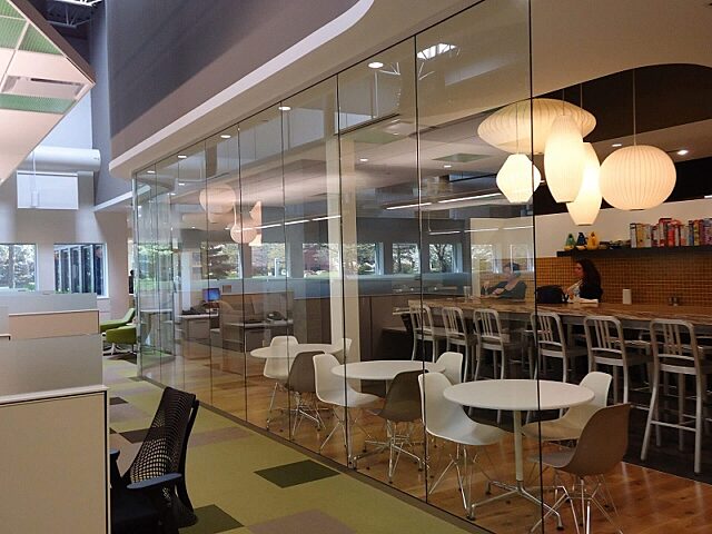 Glass Symbio walls enclose a collaborative break area with modern lighting and furniture, maintaining an open feel while separating it from workspaces.
