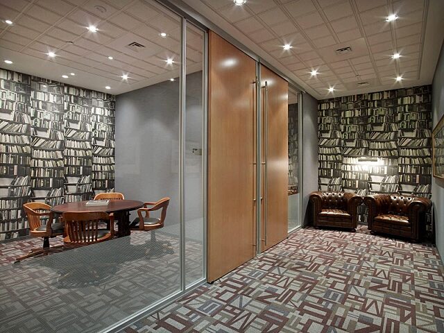 Cozy meeting space with Symbio walls, wood panel partitions, and library-themed wallpaper creating a classic ambiance, complemented by chairs and a table.