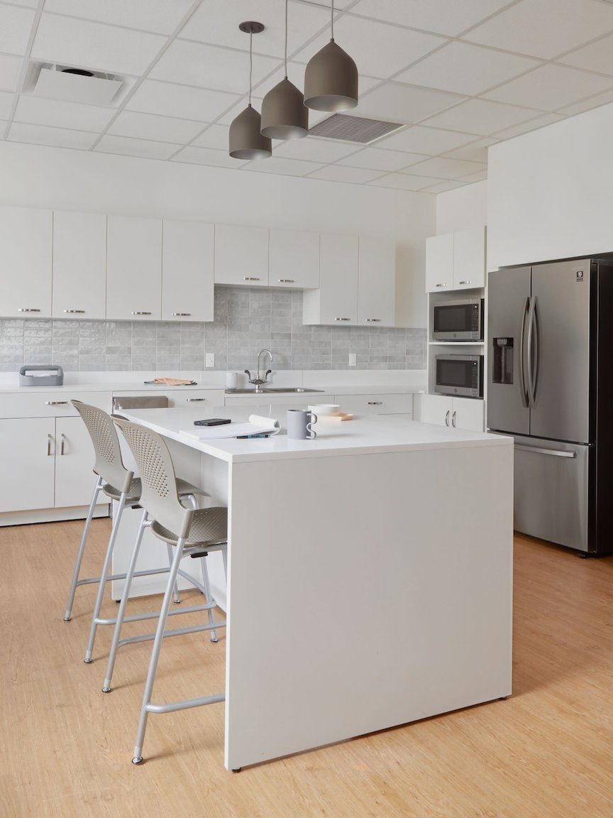 Staff break room, white laminate Mora casework along backwall & an island of white Mora casework with 2 Caper stools in Cappuccino seat/back, silver legs.