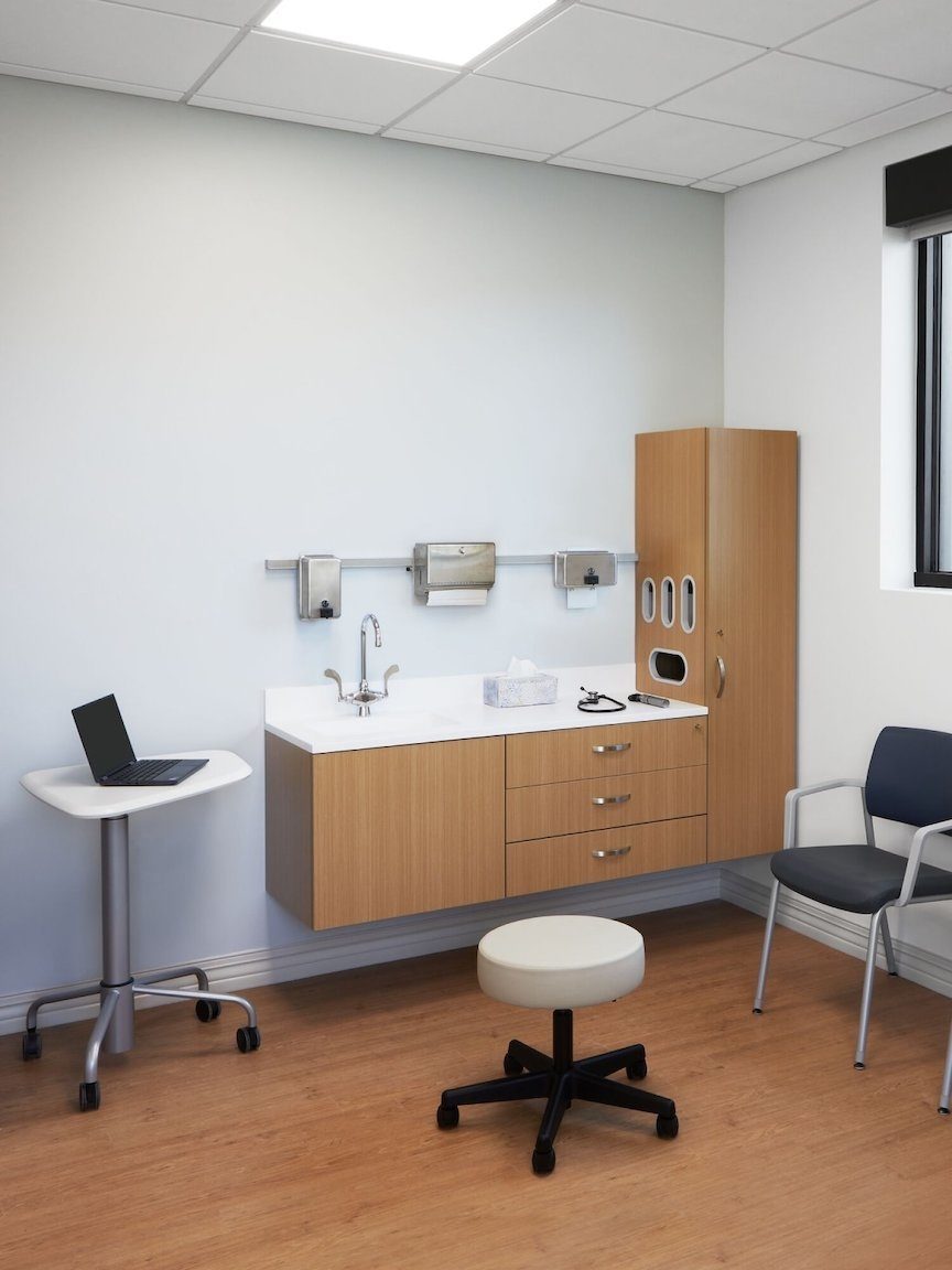 Patient exam room with Oak cabinetry, white surface, a mobile table, two dark Verus side chairs with a Nemschoff Riva bench, and a physician's stool